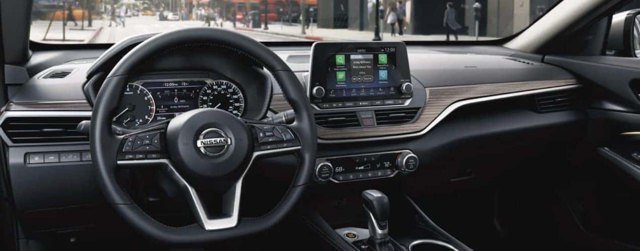 The black interior of a 2021 Nissan Altima shows the steering wheel and infotainment screen.