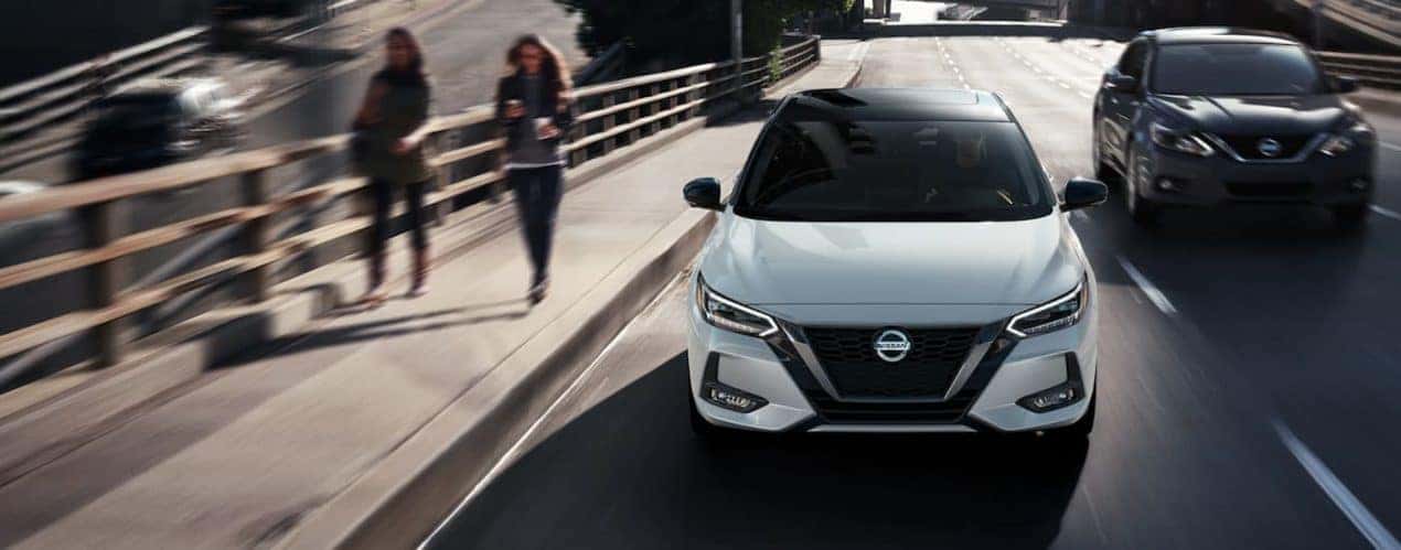 A white 2022 Nissan Sentra is shown from the front driving on a city road.