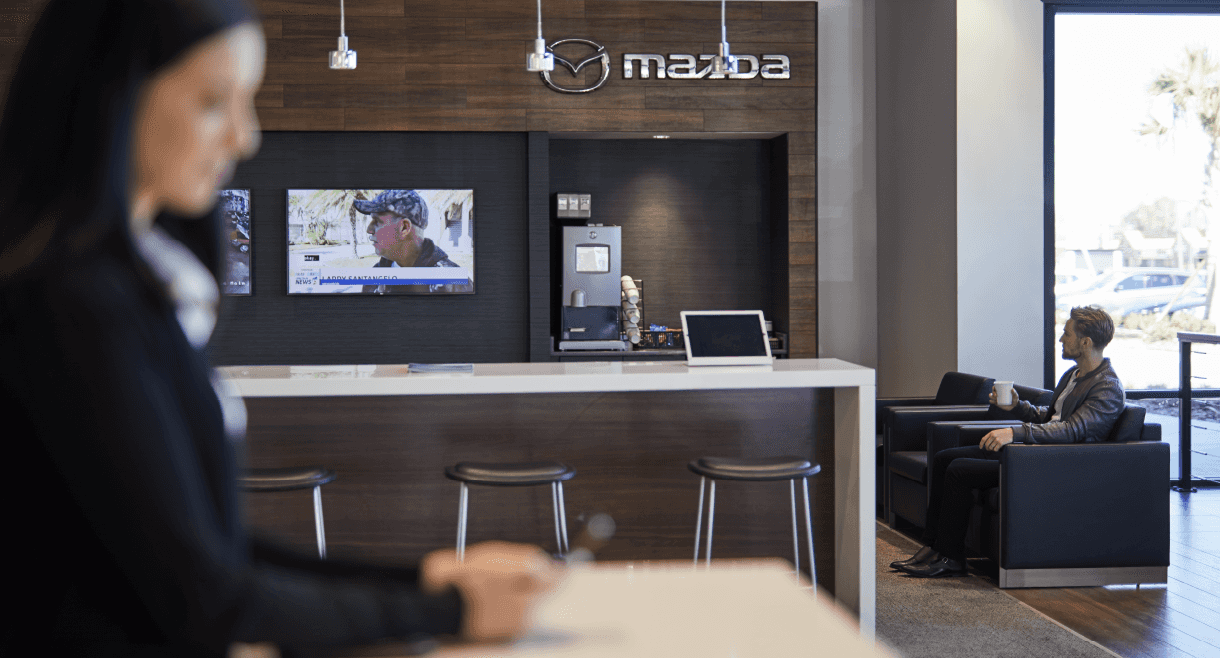 Two persons sitting in the Mazda dealership waiting area.