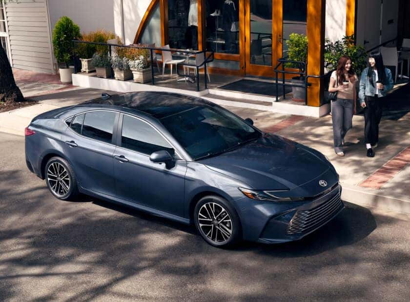 Toyota Camry XLE in Heavy Metal showcasing its sleek profile parked along an urban storefront street.