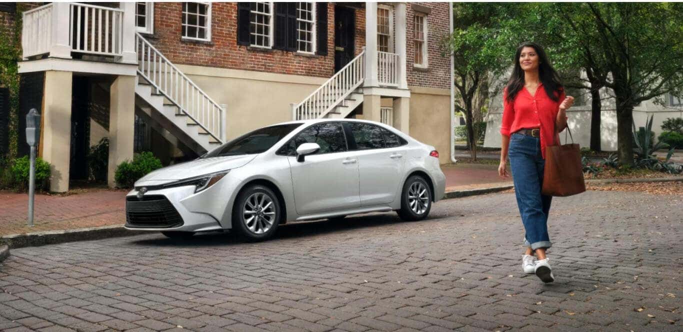 Side view of a Toyota Corolla LE parked on a brick-paved city street while a woman walks by.