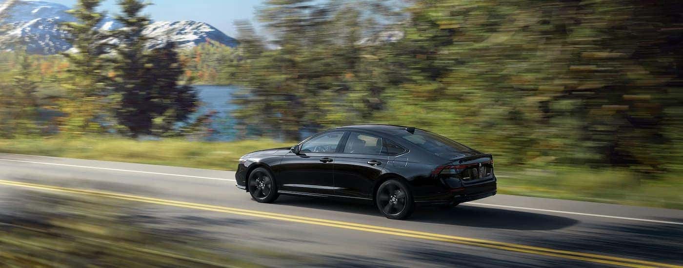 A black 2023 Honda Accord Sport-L is shown driving past a lake.