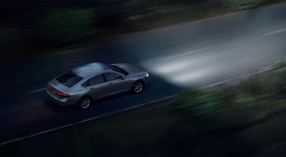 A grey 2023 Honda Accord EX is shown driving on an open road at night.
