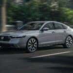 A grey 2023 Honda Accord Touring Hybrid is shown driving on a city street after leaving a Honda dealer near you.