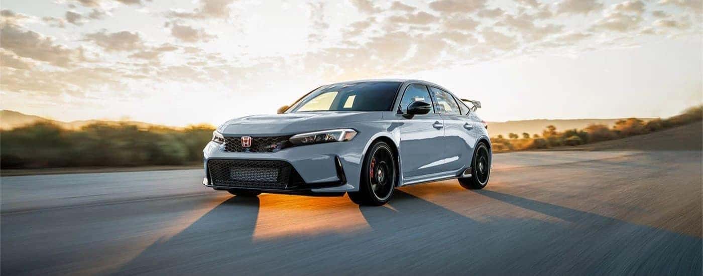 A grey 2023 Honda Civic Type R is shown driving on an open road after leaving a Honda dealer.