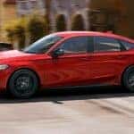 A red 2023 Honda Civic Sport is shown driving on a city street after leaving a Honda dealer near you.
