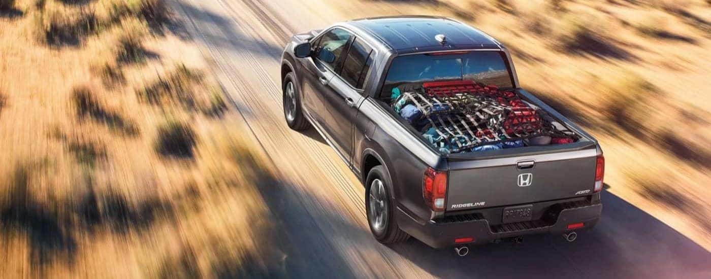 A grey 2023 Honda Ridgeline RTL-E is shown driving on a dirt path.