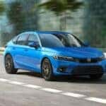 A blue 2024 Honda Civic Hatchback is shown driving to a Honda dealer near Tuttle, OK.