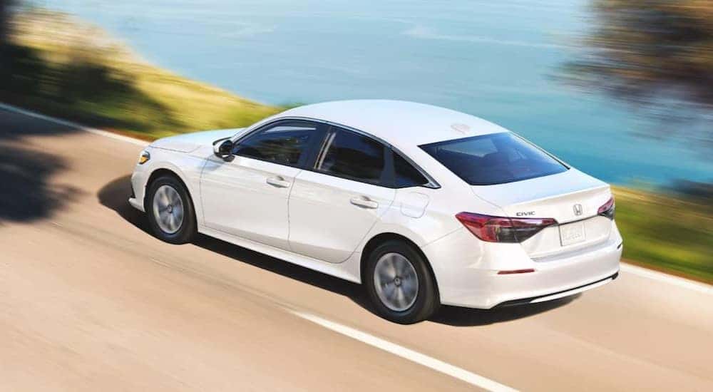 A white 2024 Honda Civic sedan is shown driving near an ocean.