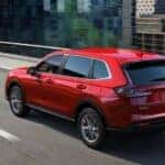 A red 2024 Honda CR-V for sale is shown driving near a city.