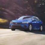 A blue 2024 Honda Civic LX driving on a winding road.