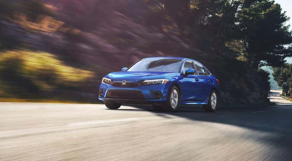 A blue 2024 Honda Civic LX driving on a winding road.