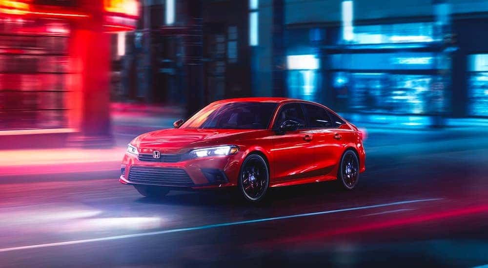 A red 2024 Honda Civic Sport driving past neon lights at night.