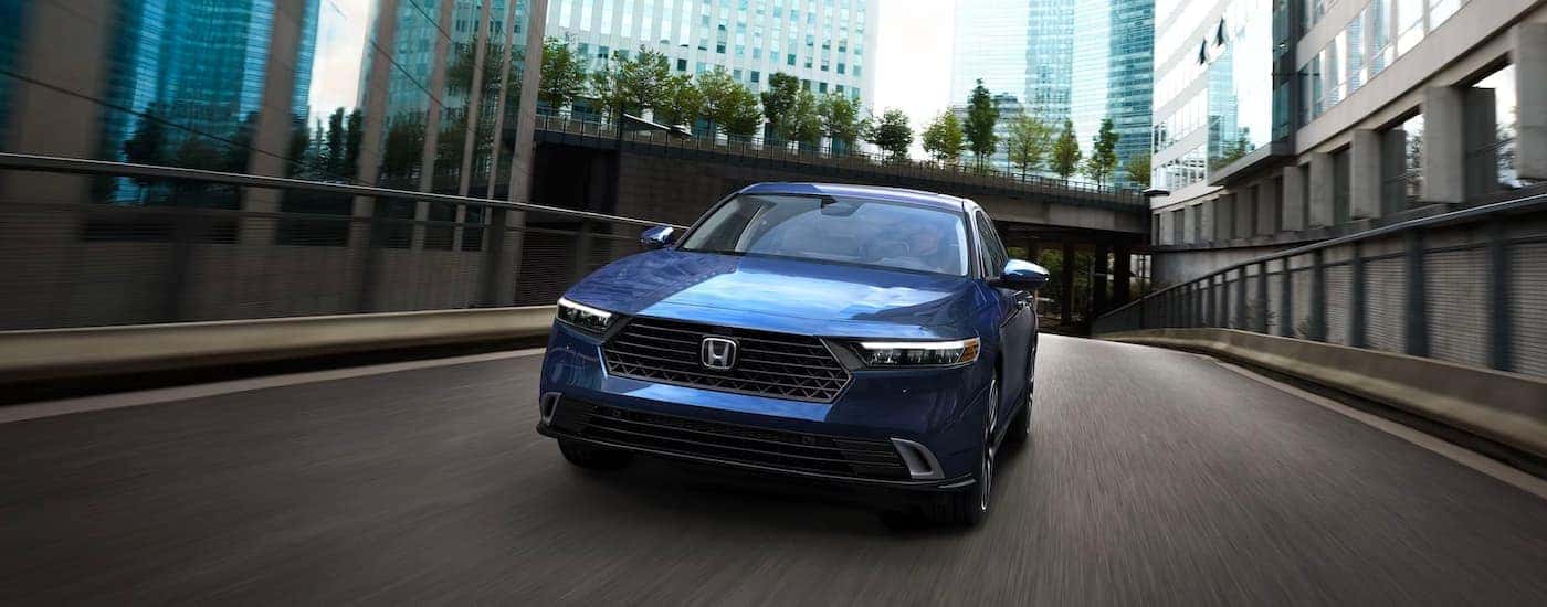 A blue 2023 Honda Accord Sport Hybrid is shown driving on a city street.
