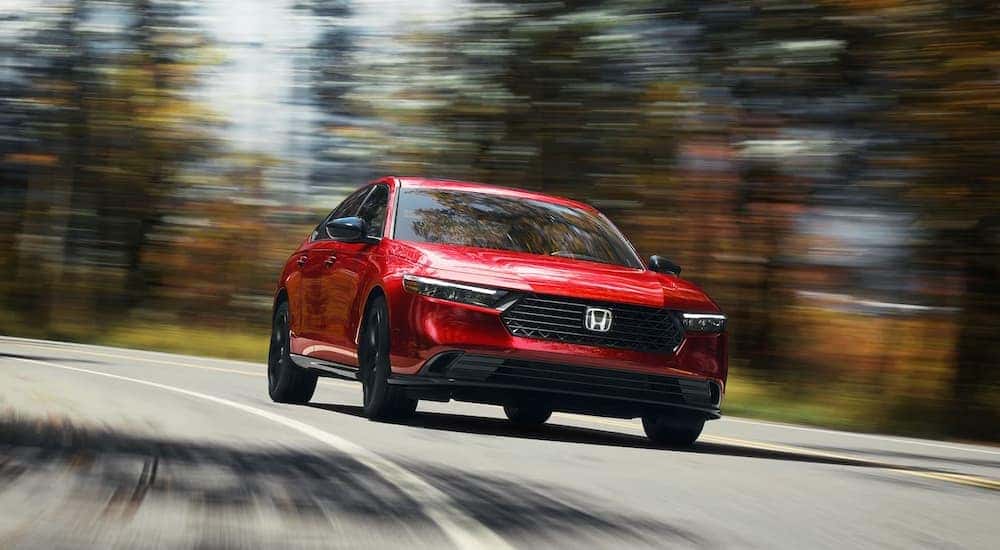 A red 2024 Honda Accord Sport-L Hybrid is shown driving on a highway.