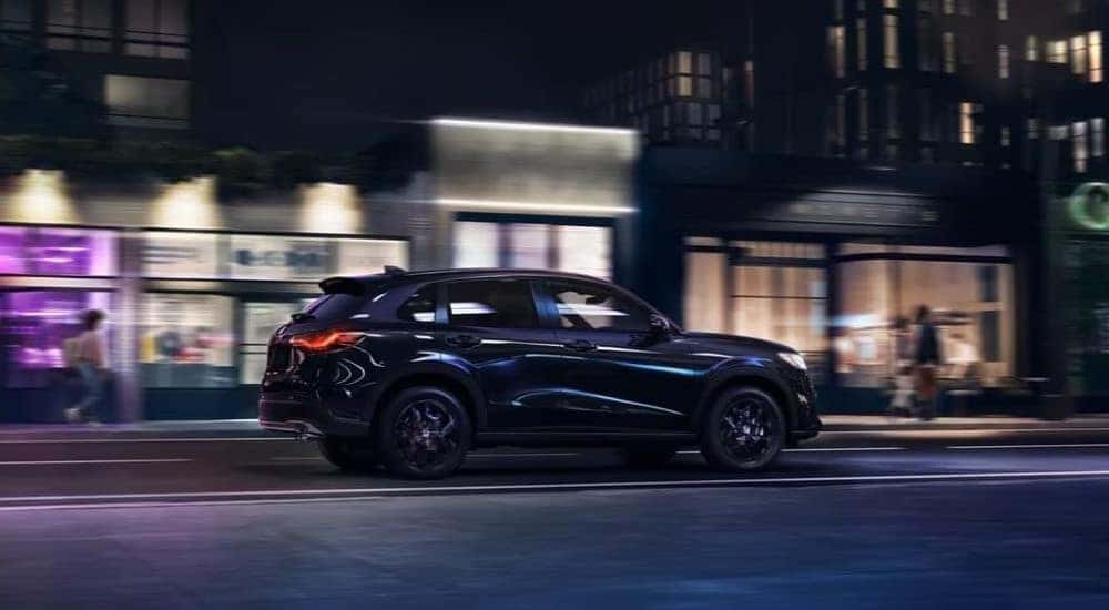 A dark blue 2025 Honda HR-V Sport driving past neon lights at night.