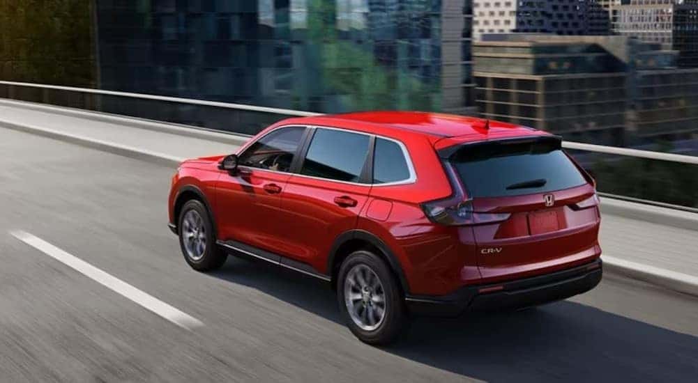 A red 2023 Honda CR-V is shown driving to visit a used Honda dealer.