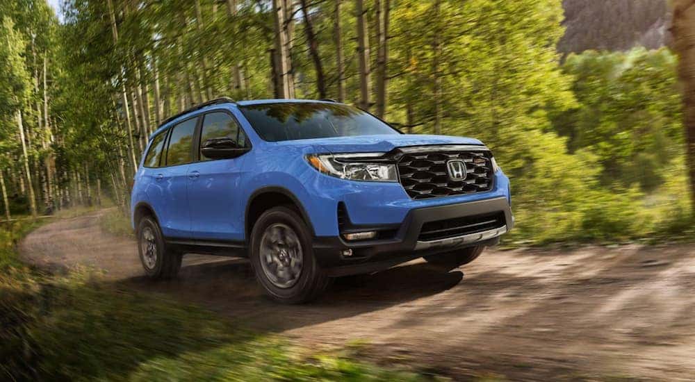 A blue 2024 Honda Passport TrailSport driving on a wooded trail.