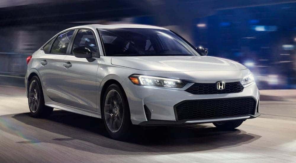 A white 2025 Honda Civic Sport Hybrid driving in a city and angled right.