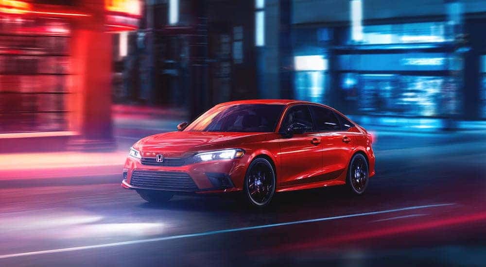 A red 2025 Honda Civic Sport Touring Hybrid driving through a city at night.