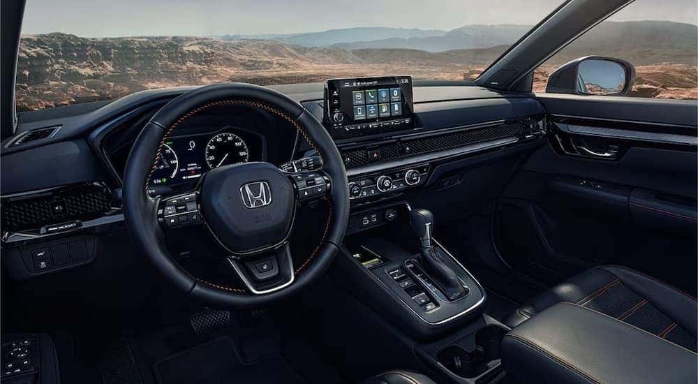The black interior of a 2025 Honda CR-V is shown from the driver's side.