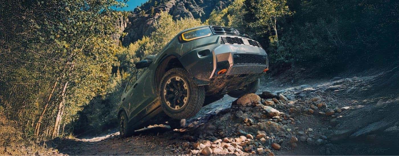 Low angle view of a green 2026 Honda Passport TrailSport off-roading over large rocks.