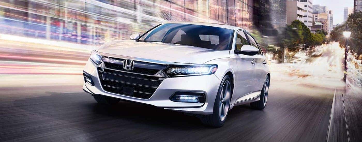 A white 2020 Honda Accord Touring driving from a dealer with a used Honda Accord for sale.