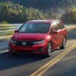A red 2025 Honda Odyssey driving down a road.