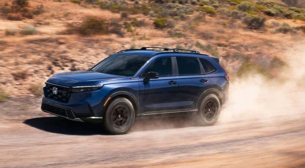 A blue 2026 Honda CR-V TrailSport Hybrid driving on a dirt road.
