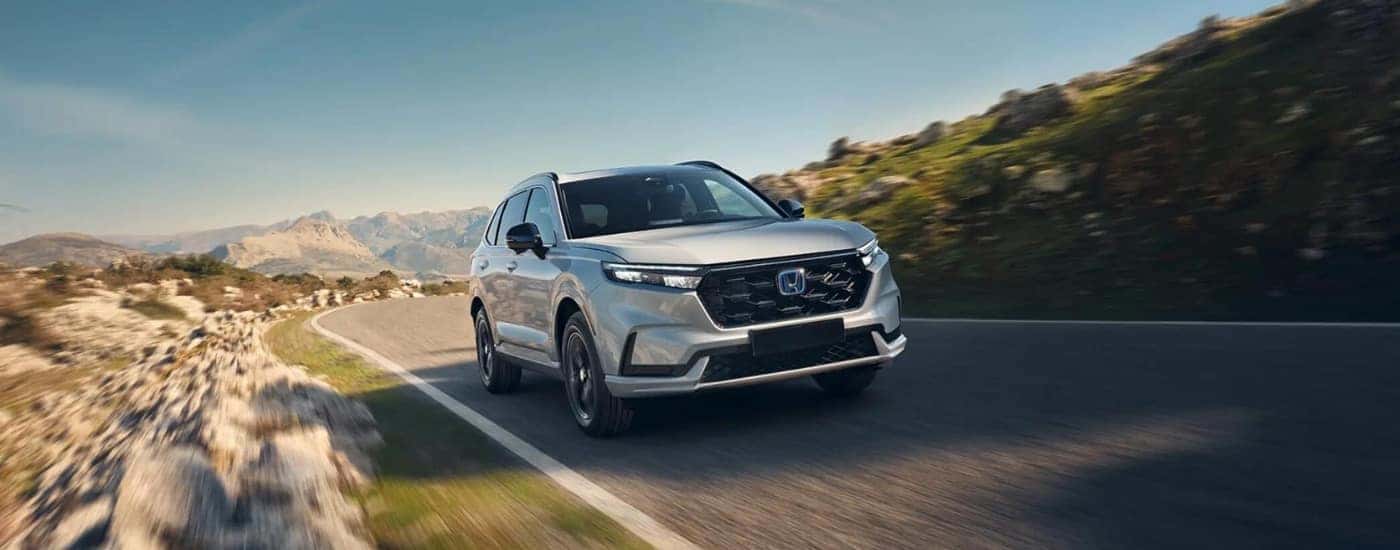 A white 2025 Honda CR-V Hybrid driving down a highway