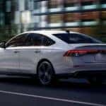 A white 2025 Honda Accord Hybrid driving in a city.