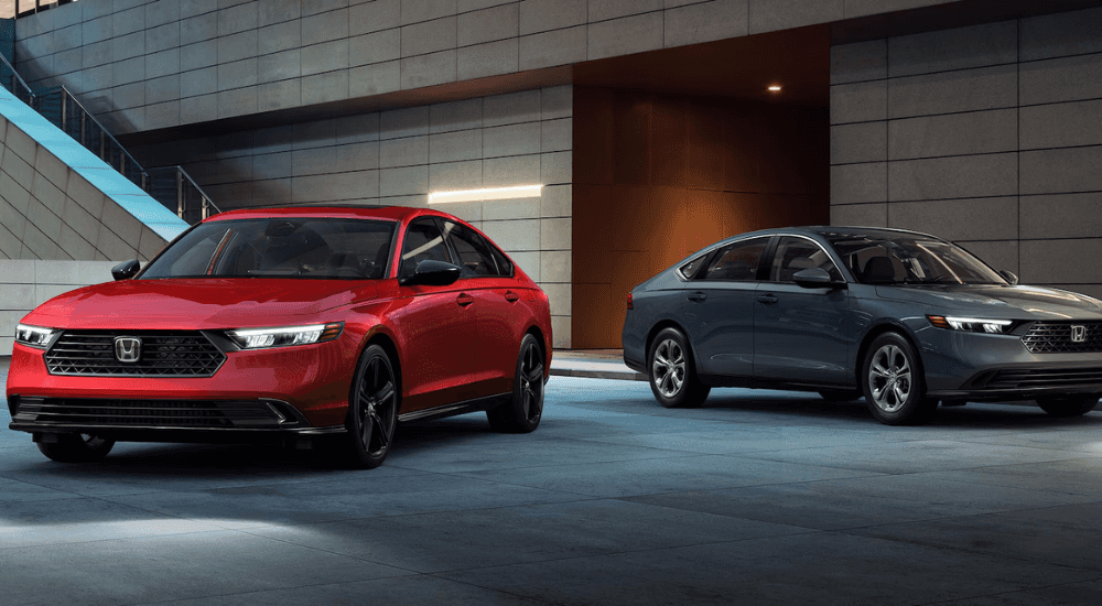 Two 2025 Honda Accord's, one red one grey, parked side by side at an angle underneath an overhand.