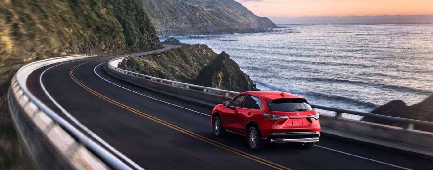 Rear of a red 2023 Honda HR-V EX-L driving towards a bend.