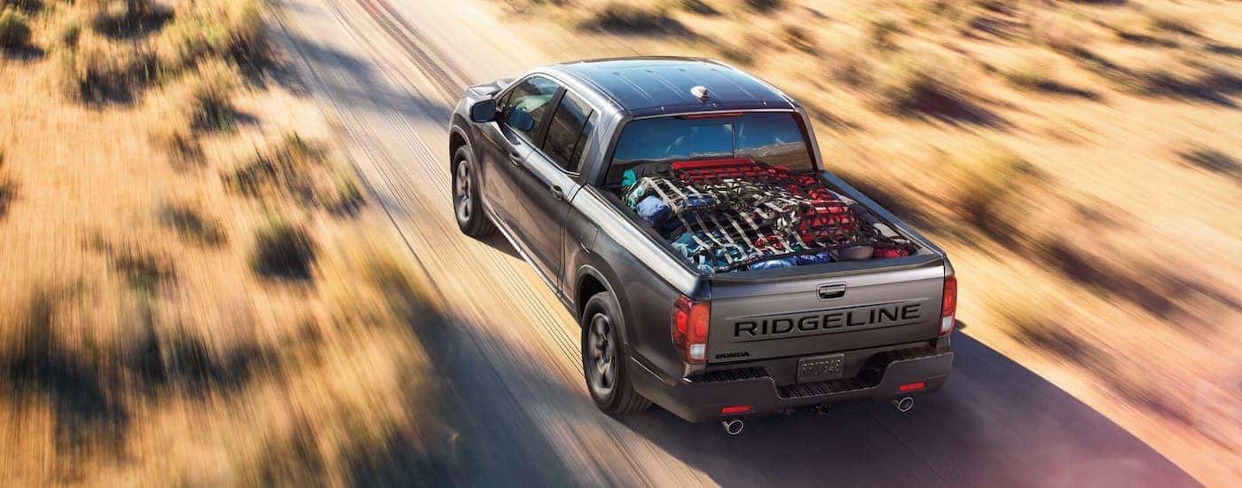 High rear view of a grey 2026 Honda Ridgeline driving down a road.