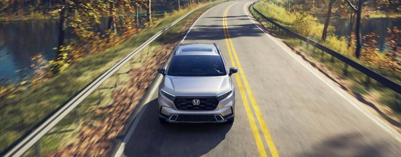 Front of a white 2026 Honda CR-V Hybrid driving down a road.