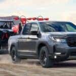 A gray 2026 Honda Ridgeline towing a side by side and dirt bikes.
