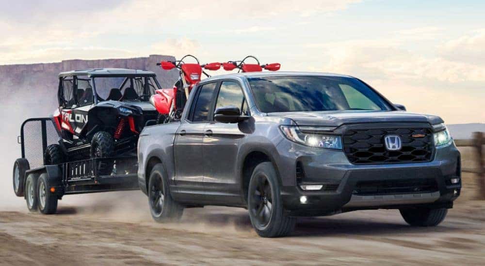 A gray 2026 Honda Ridgeline towing a side by side and dirt bikes.
