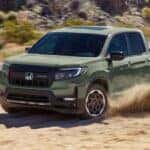A light green 2026 Honda Ridgeline shown driving on a sandy road.