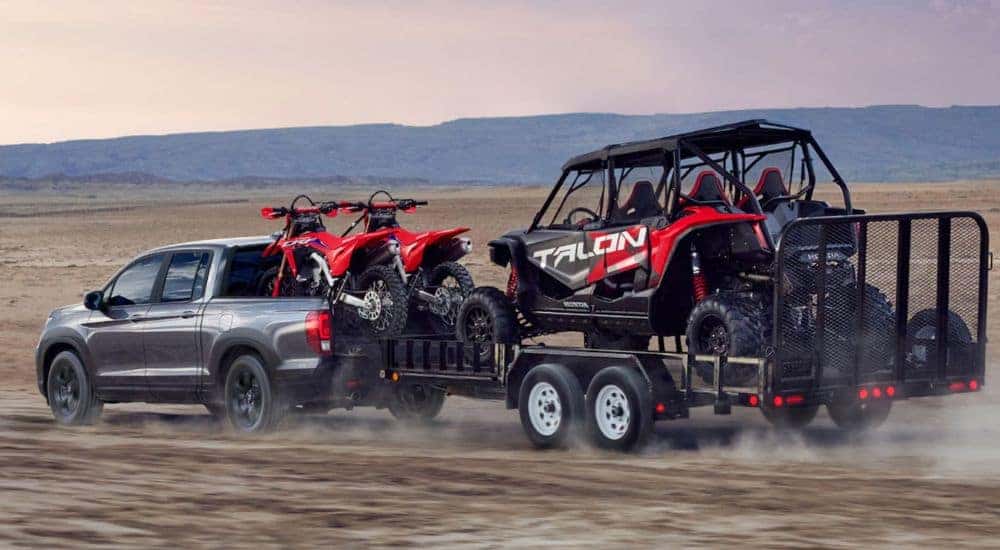 Side view of a gray 2026 Honda Ridgeline towing dirt bikes and a side by side.