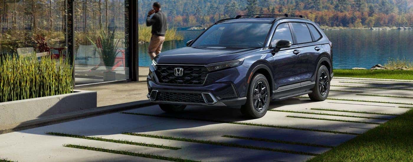 Blue 2026 Honda CR-V parked in a driveway near a mountain and lake.