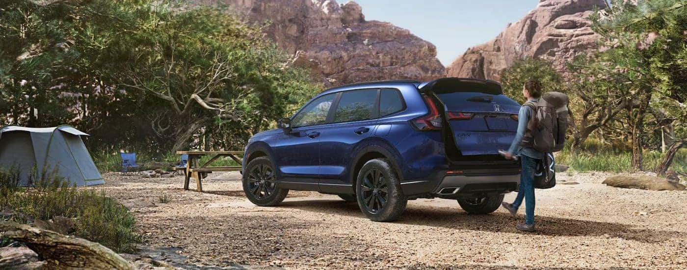 Blue 2026 Honda CR-V with a woman using the foot activated liftgate while parked at a campsite.