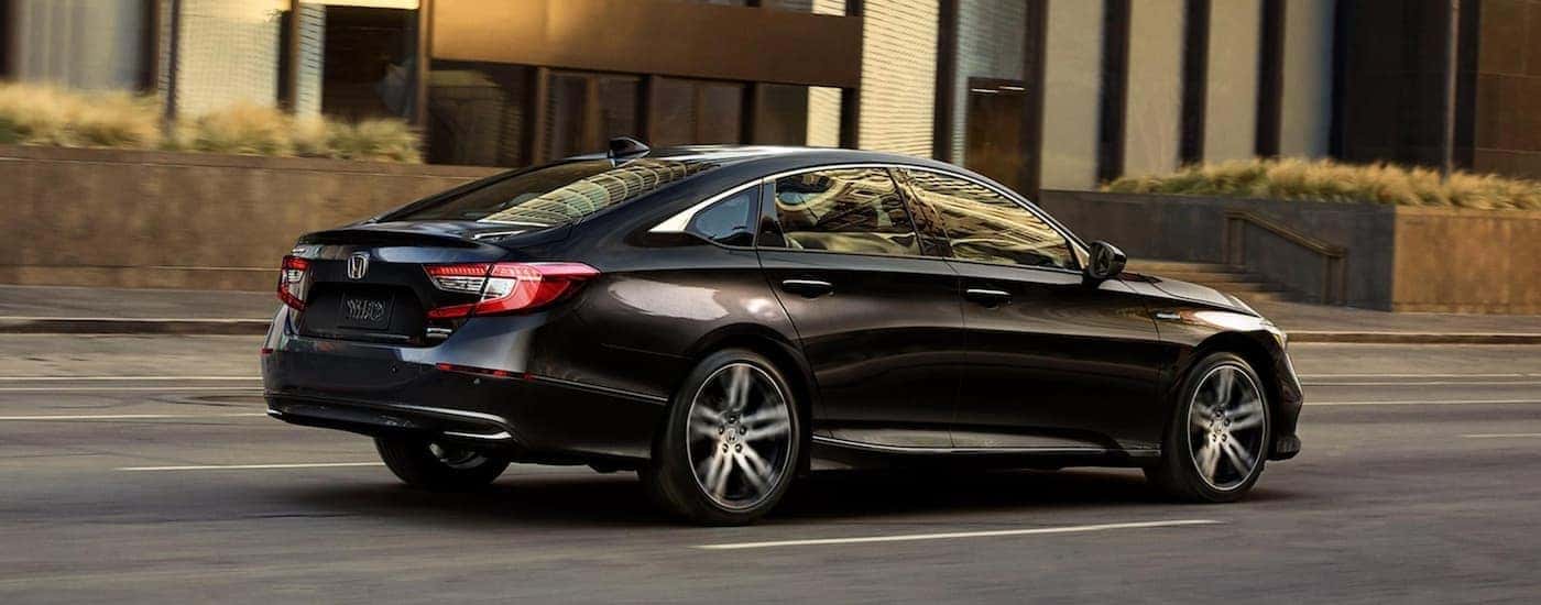 A black 2021 Honda Accord Hybrid driving by a building.