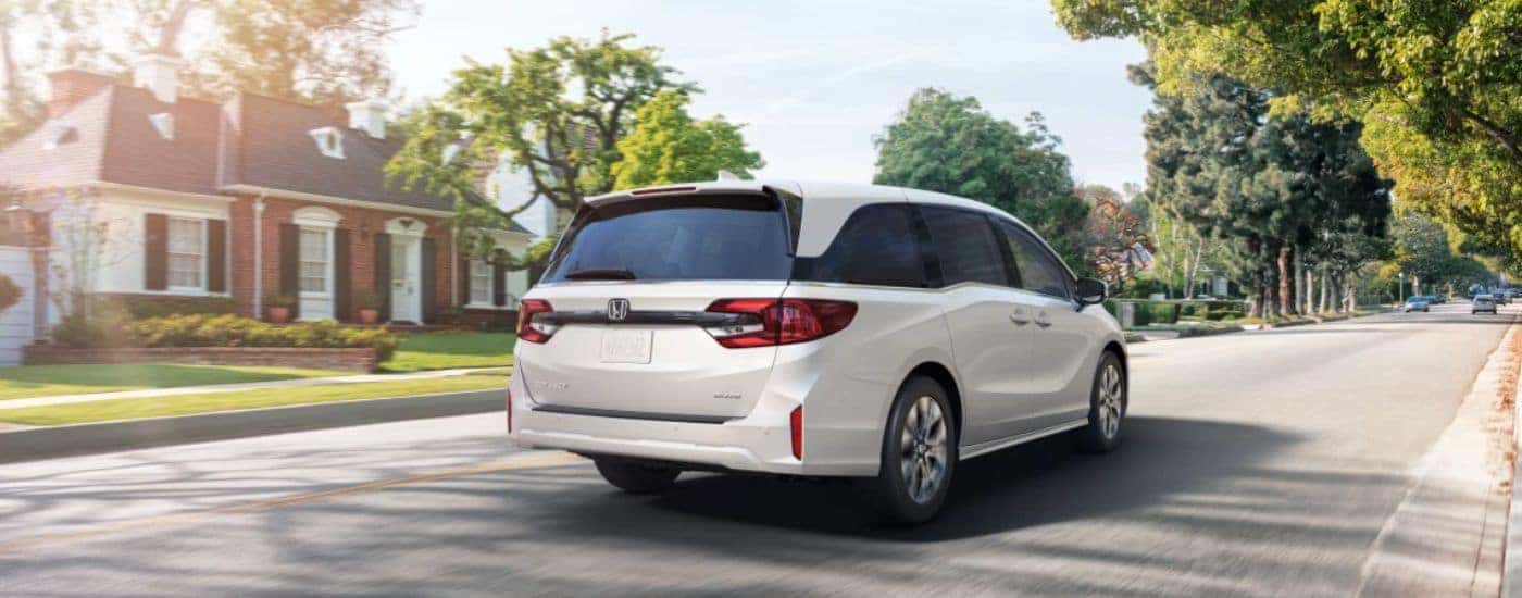 Rear view of a white 2026 Honda Odyssey driving down a residential street.