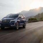 A blue 2022 Chevy Equinox is driving past mountains and a setting sun.