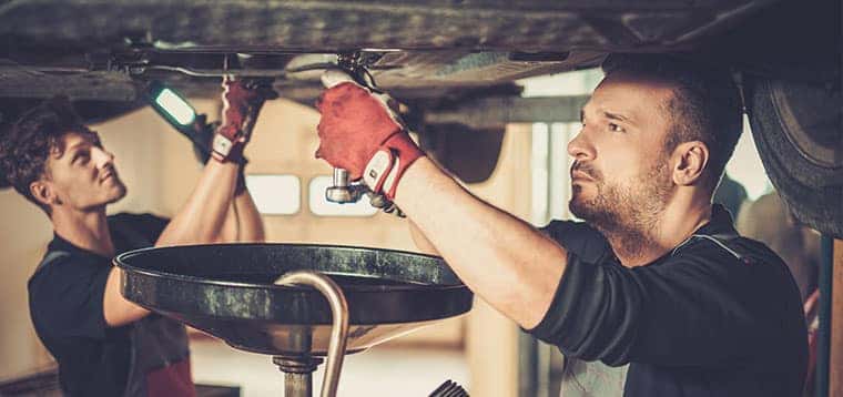 Service technicians performing vehicle maintenance under a vehicle on a lift.
