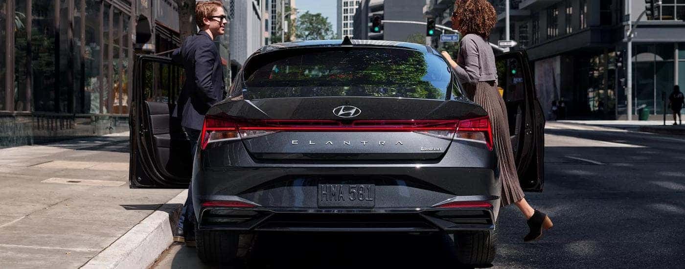 Two people are getting into the front seats of a gray 2022 Hyundai Elantra Limited.