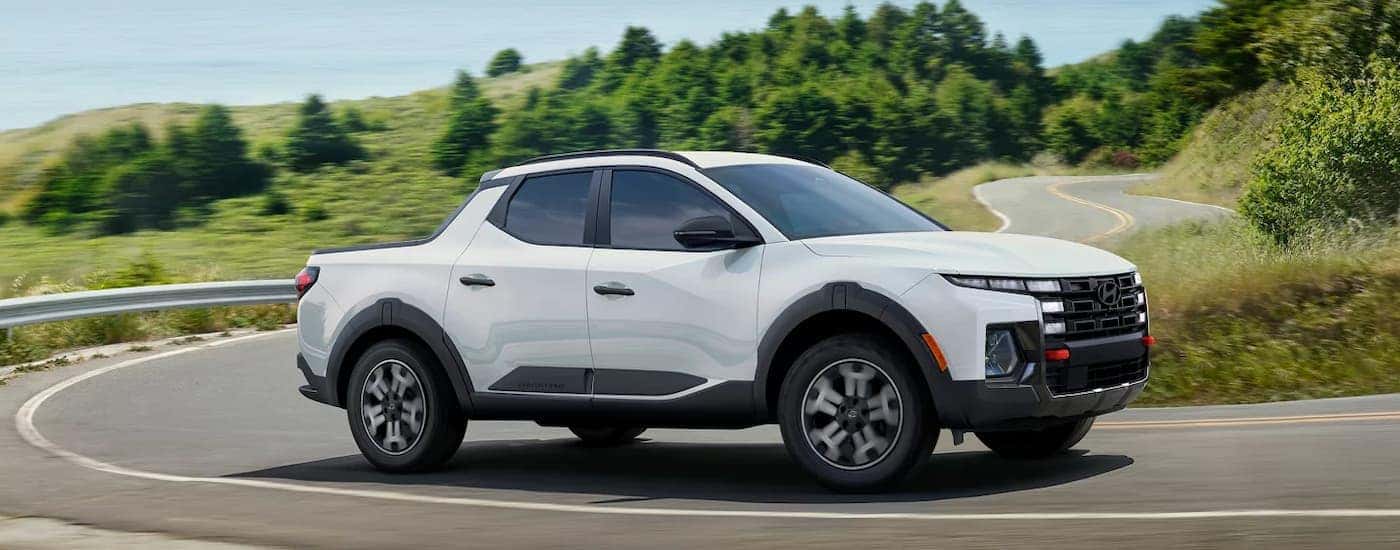 A white 2025 Hyundai Santa Cruz XRT driving on a winding highway corner.