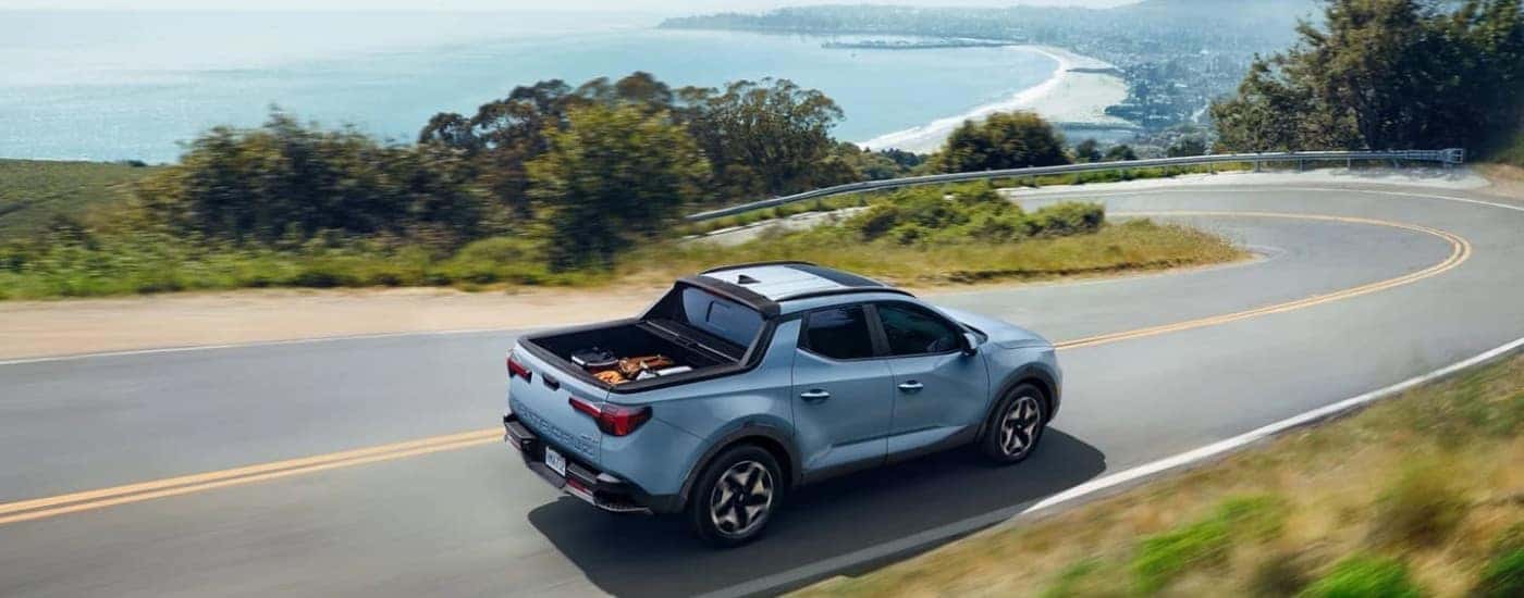 A popular used Hyundai for sale, a blue 2022 Hyundai Santa Cruz, is driving on a coastal road.