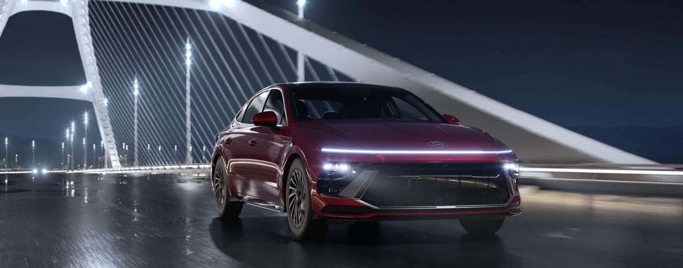 A red 2025 Hyundai Sonata Limited Hybrid driving on a bridge at night