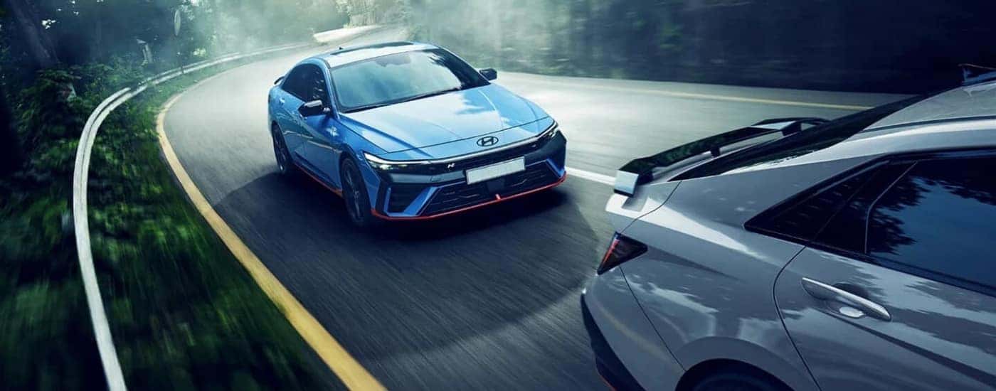 Blue 2024 Hyundai Elantra N for sale driving down a winding road.